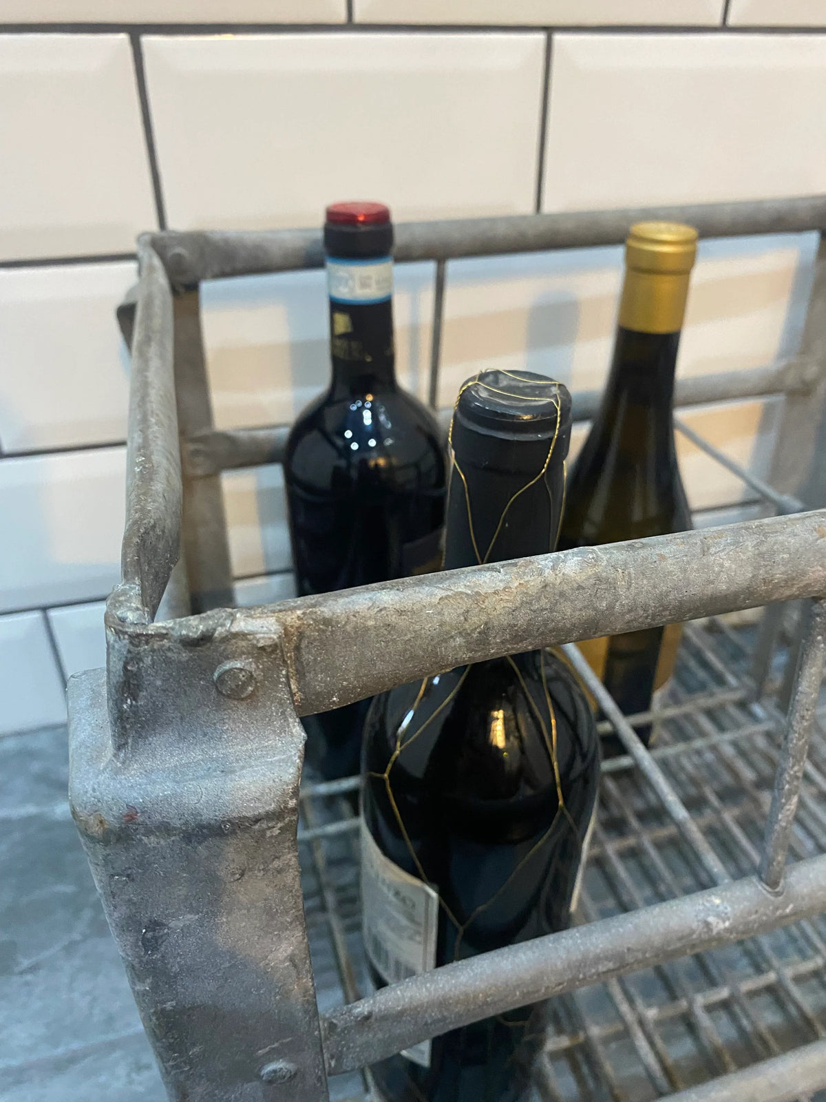 Vintage metal wine rack with three wine bottles against white tiled wall, decorative antique interior