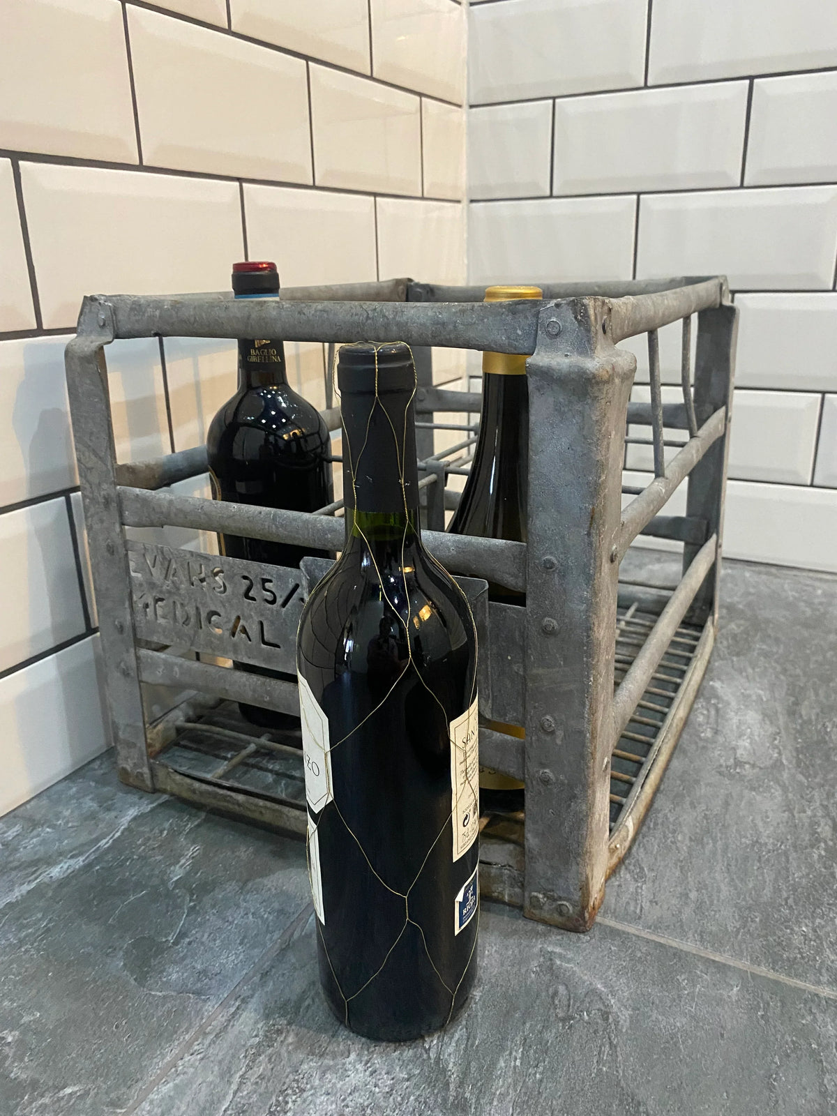 Vintage metal wine crate with bottles on tiled kitchen counter, decorative antique style