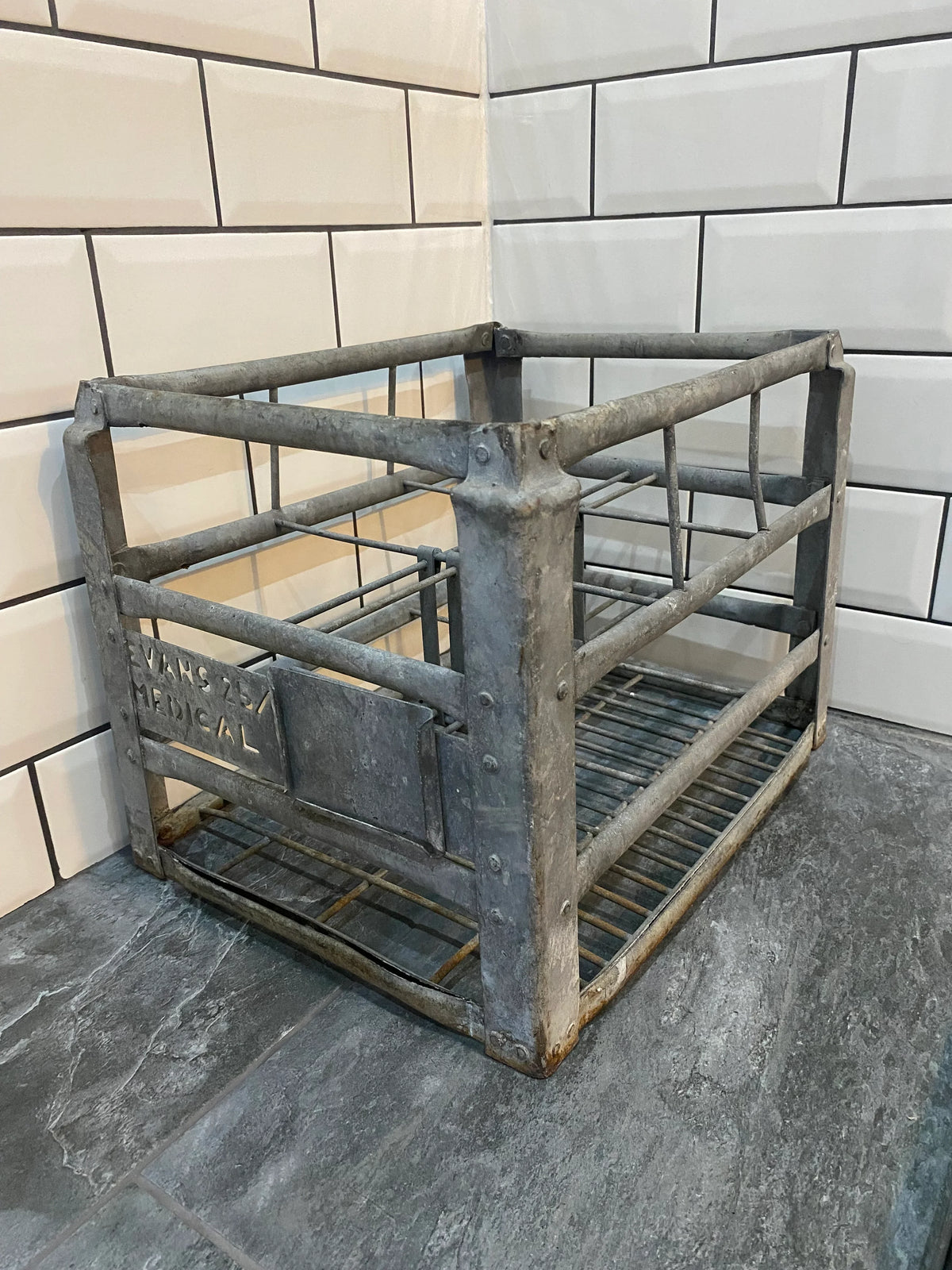 Vintage industrial metal crate with wire frame and EVANS MEDICAL label on tile floor