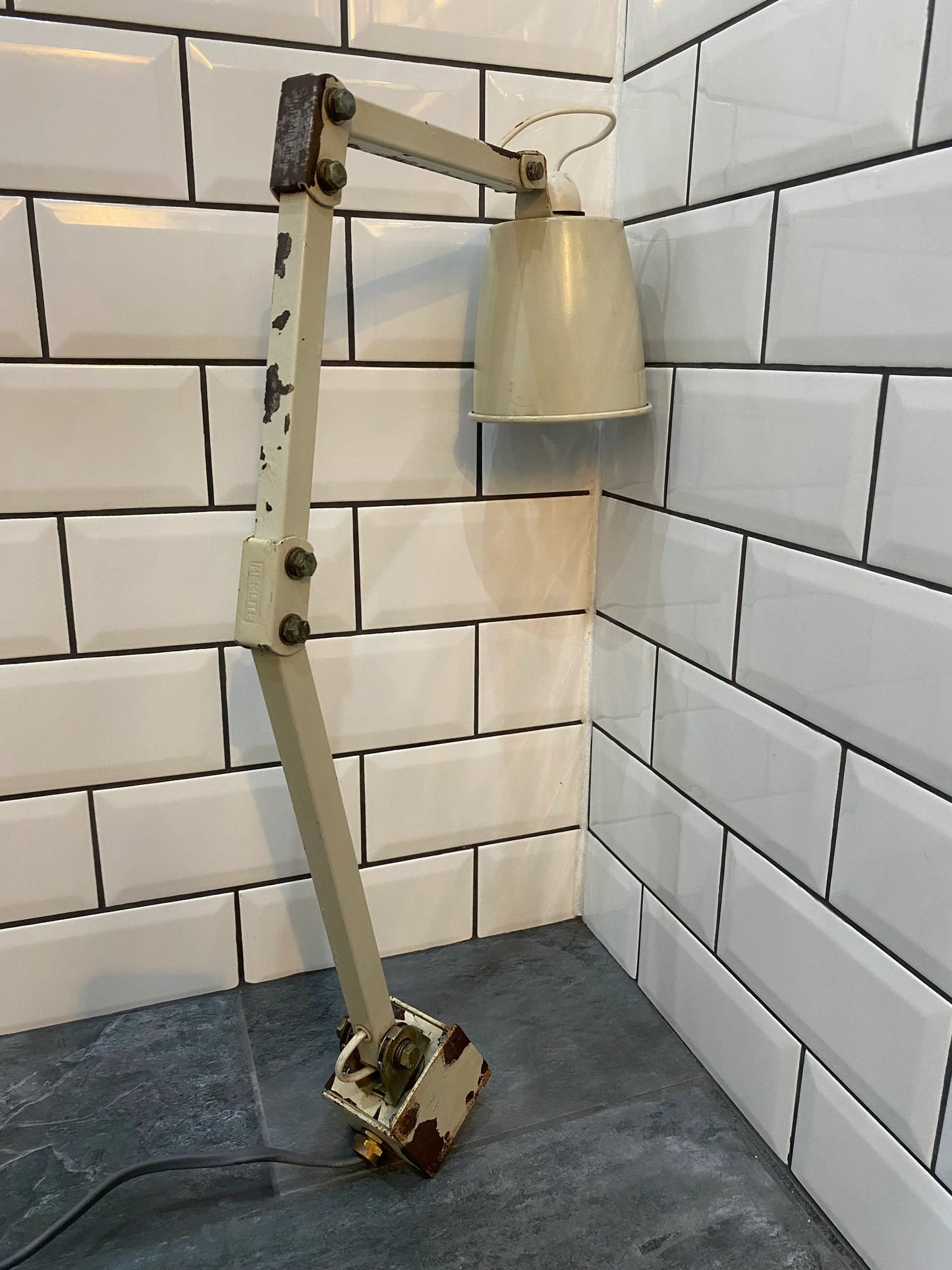 Vintage industrial adjustable desk lamp with patina on tile backsplash and stone surface.