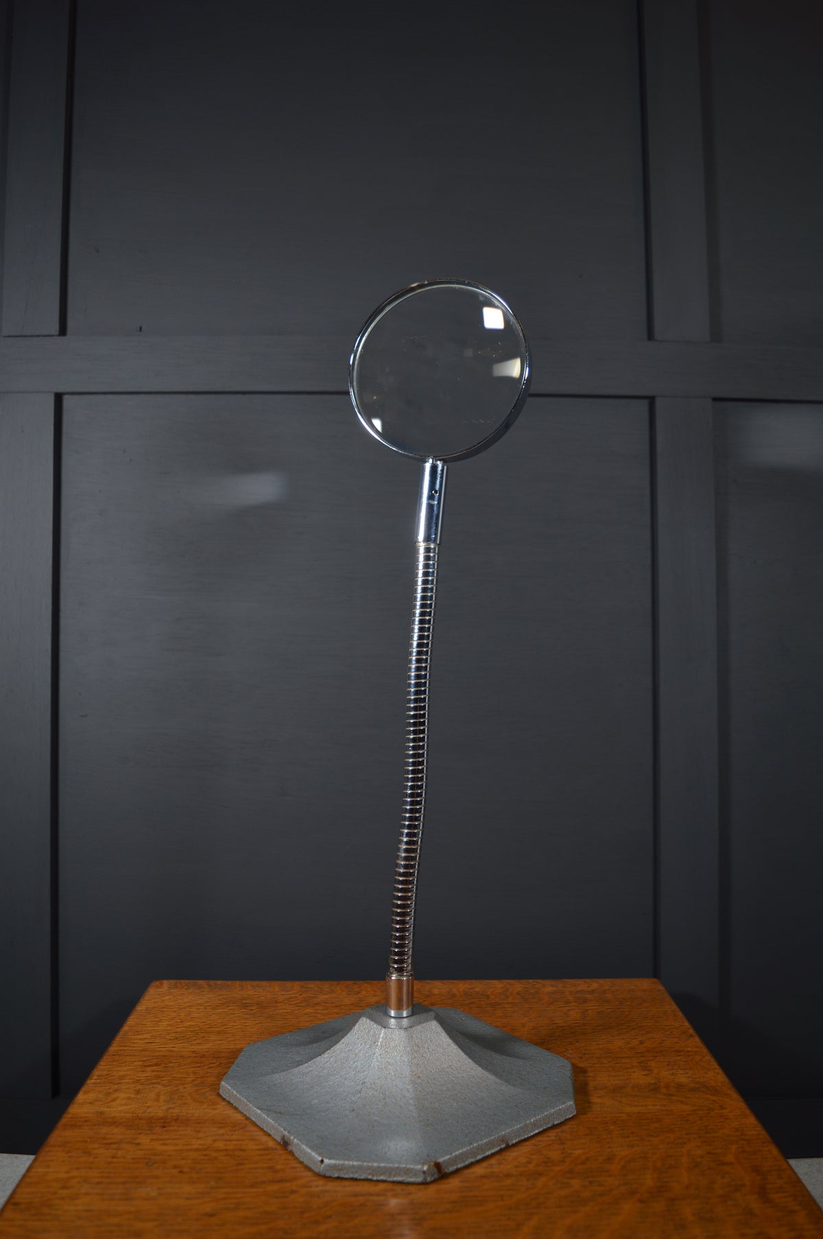 Vintage magnifying glass with adjustable metal stand on wooden table, black panel background