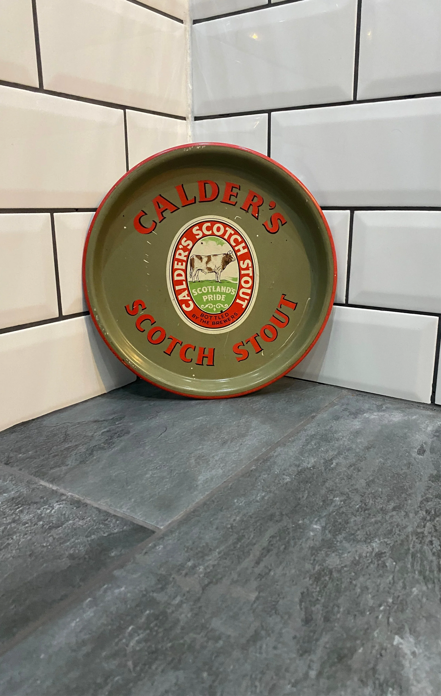 Vintage Calder's Scotch Stout metal tray on tiled floor against subway tile wall