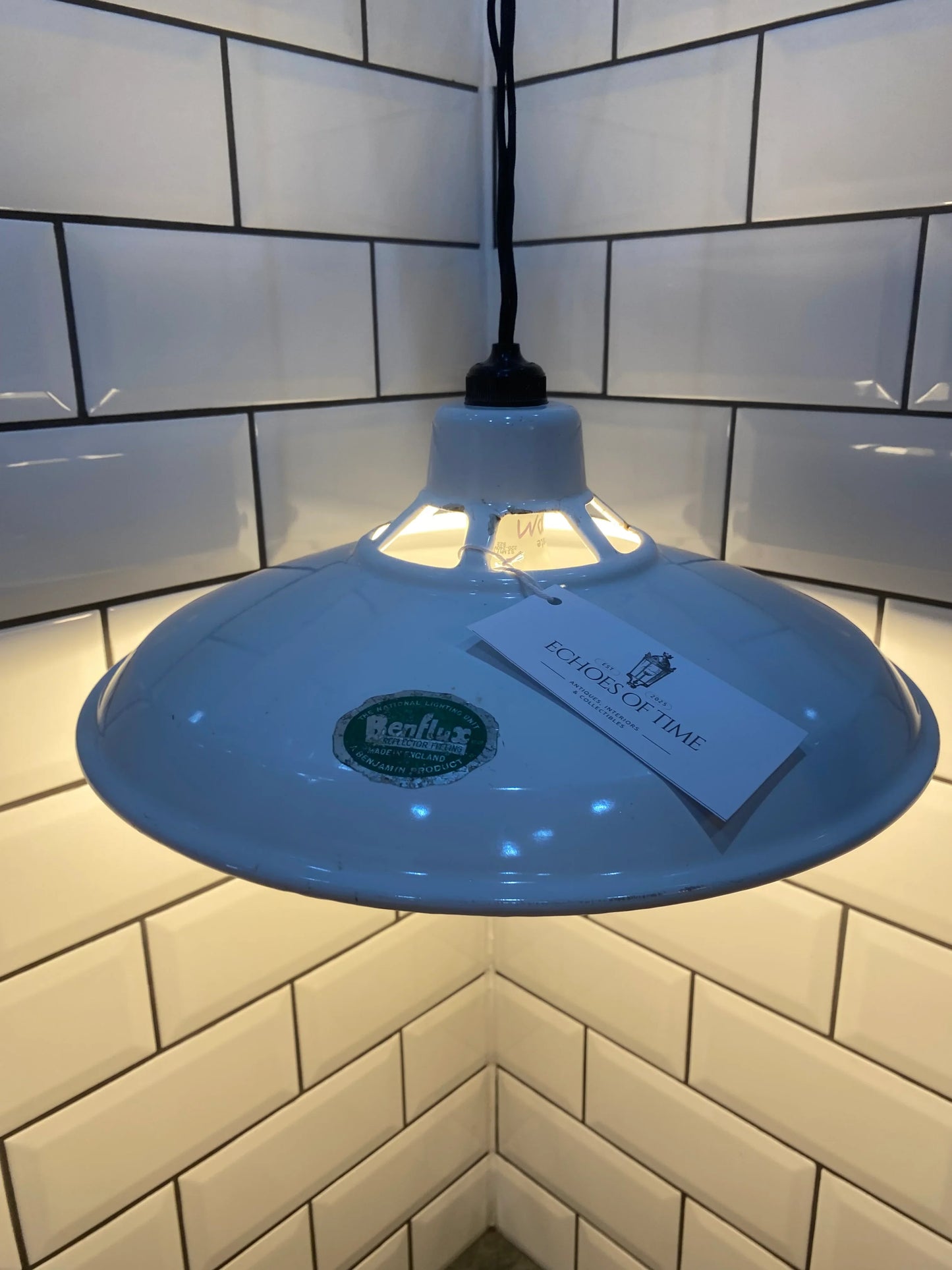 Vintage industrial pendant light with white enamel shade against subway tile wall
