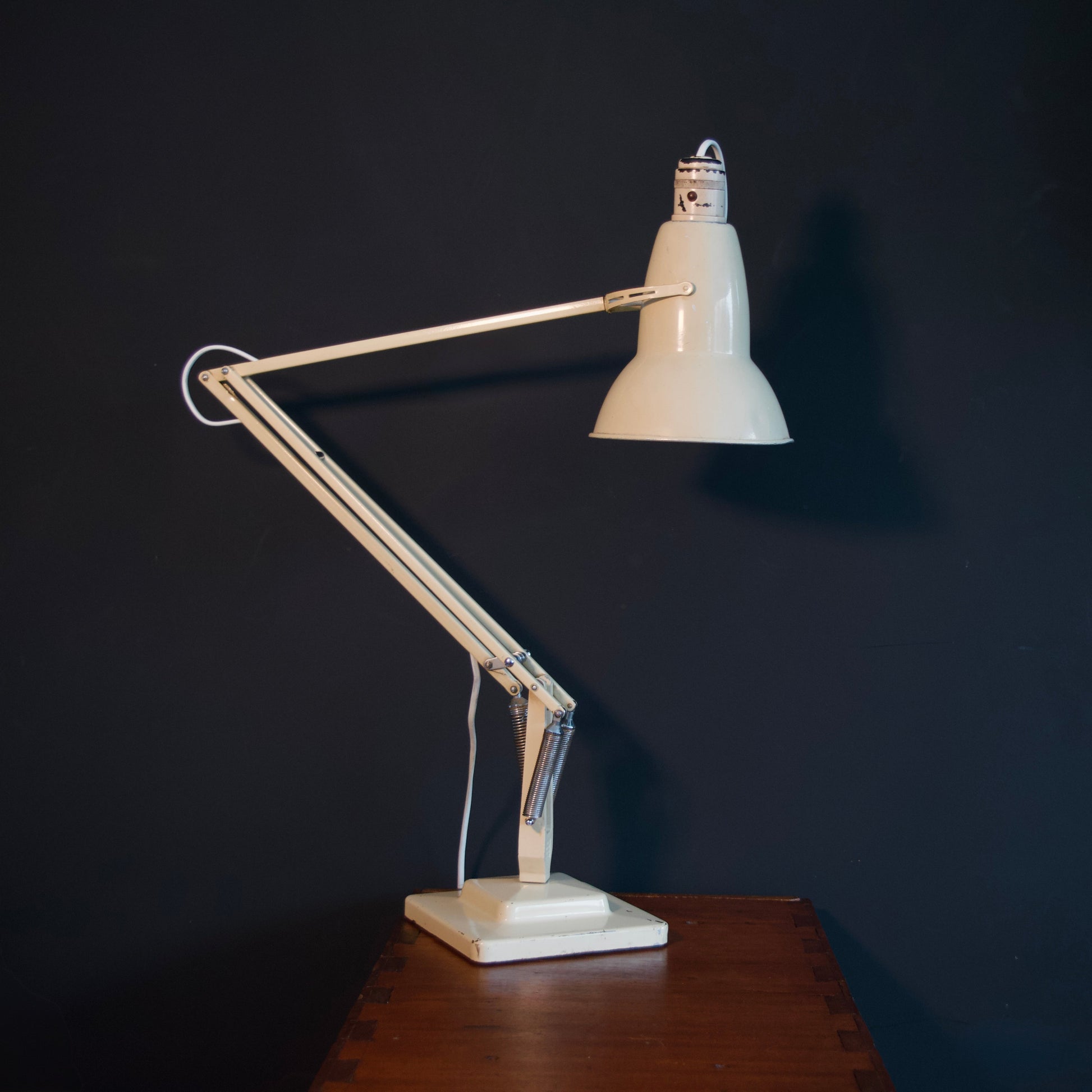 Vintage cream adjustable desk lamp on a wooden table against a dark wall