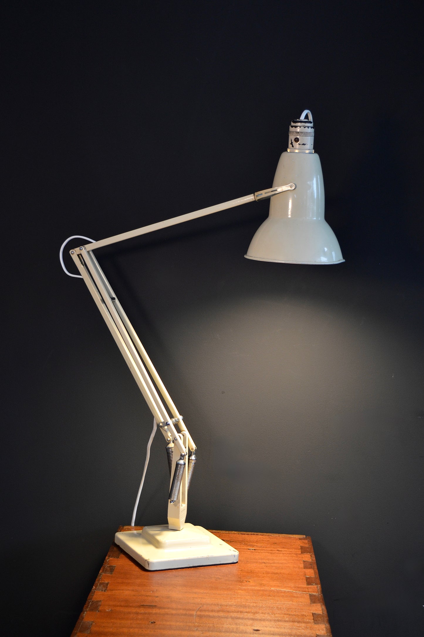 Vintage cream metal adjustable desk lamp on wooden table against dark wall