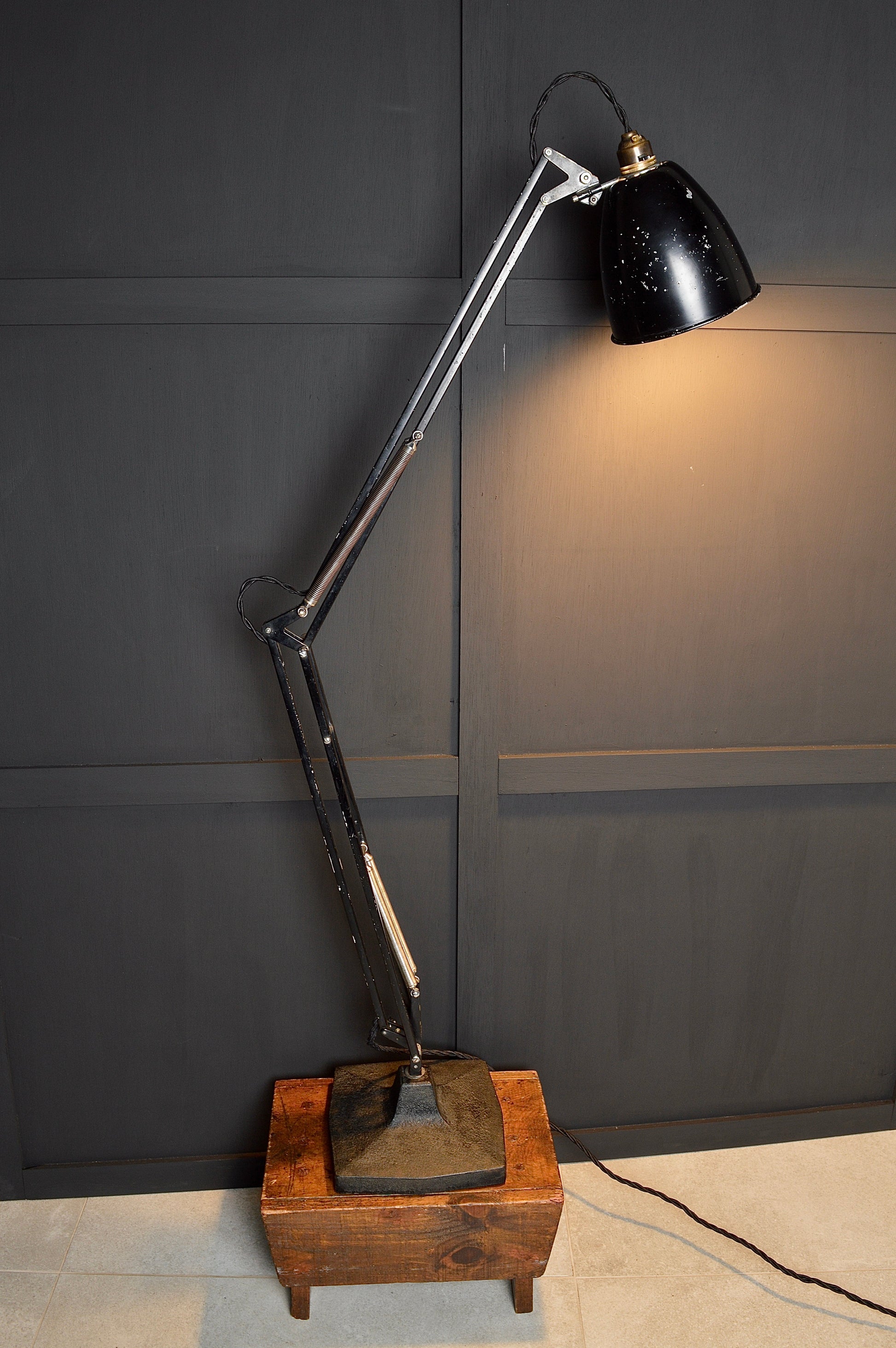 Vintage-style floor lamp with black shade and wooden base against a dark wall.