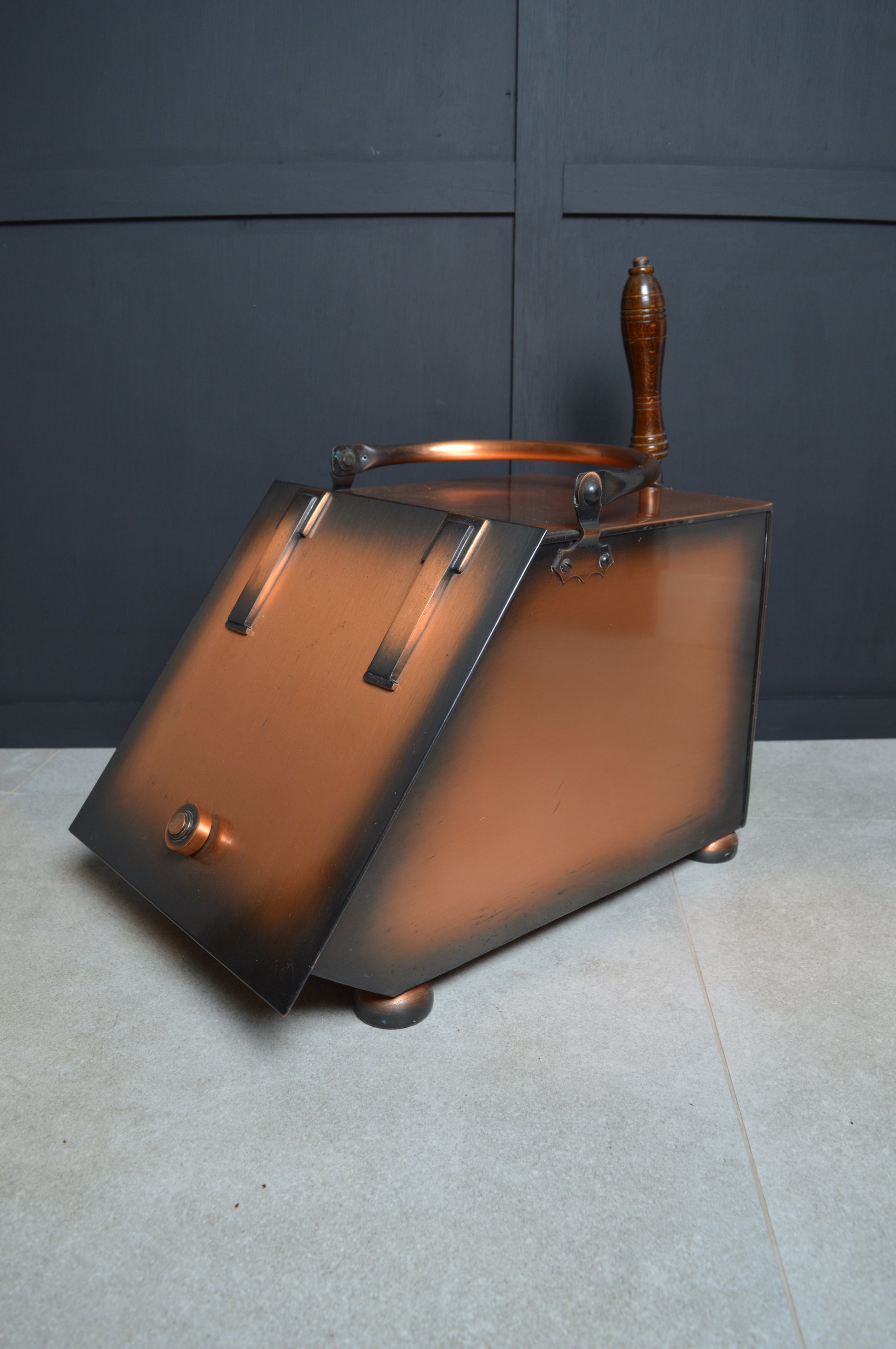 Vintage copper coal scuttle with wooden handle on a tiled floor, decorative antique home accessory