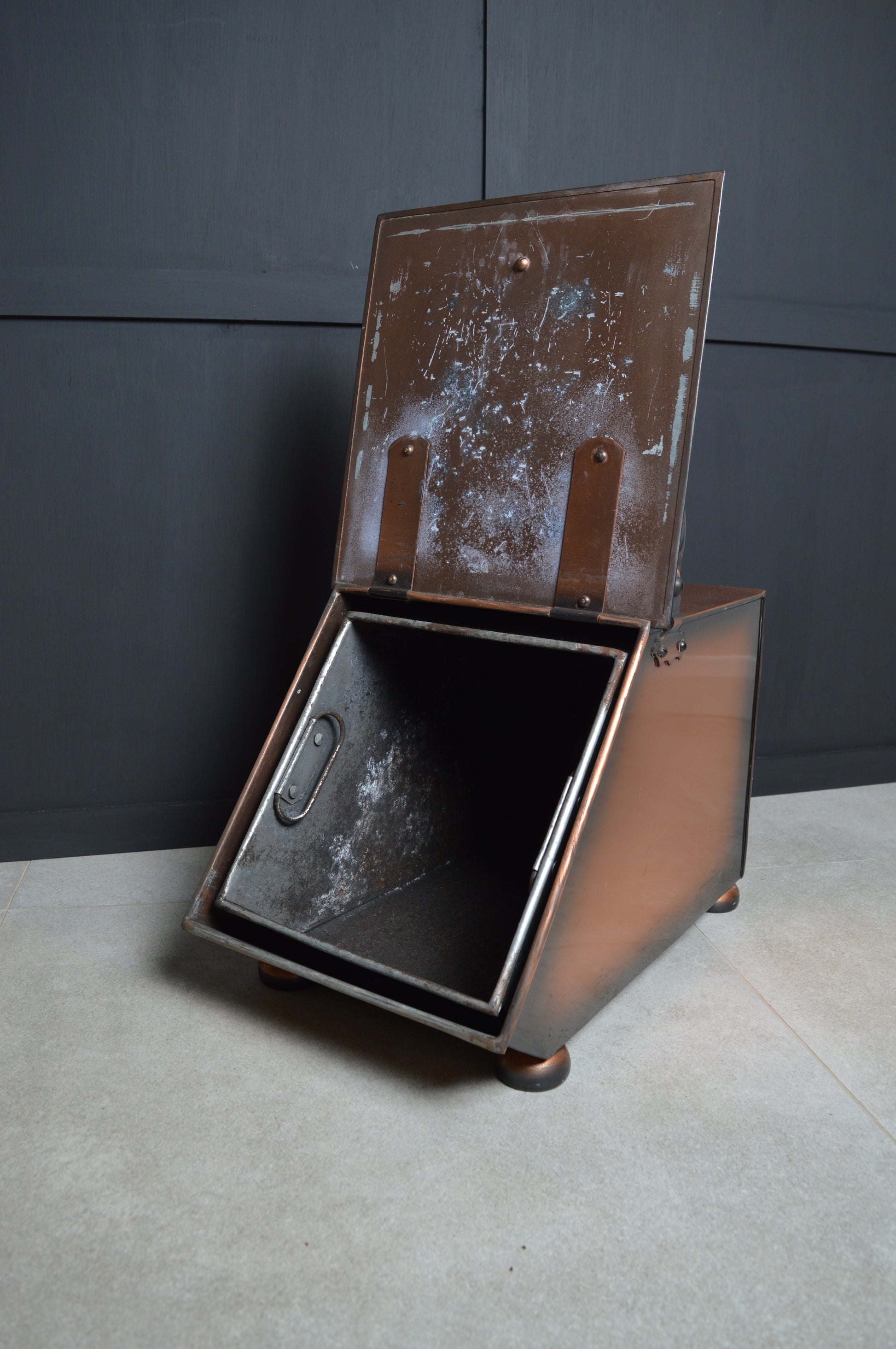 Vintage metal coal scuttle with hinged lid and aged patina on tiled floor