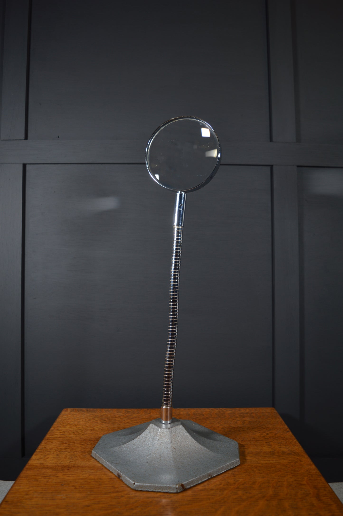 Vintage magnifying glass with adjustable metal stand on wooden table, black panel background