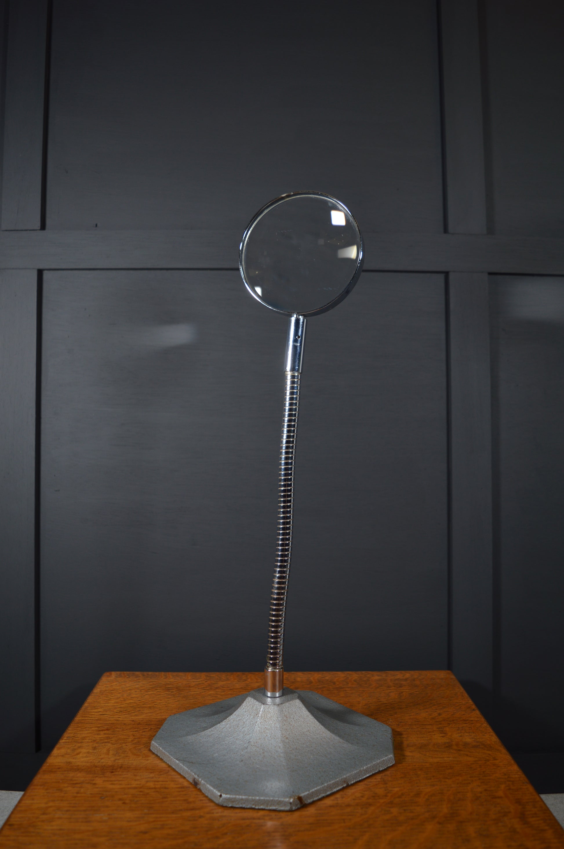 Vintage magnifying glass with adjustable metal stand on wooden table, black panel background