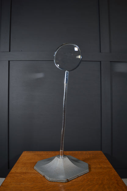 Vintage magnifying glass with adjustable metal stand on wooden table, black panel background