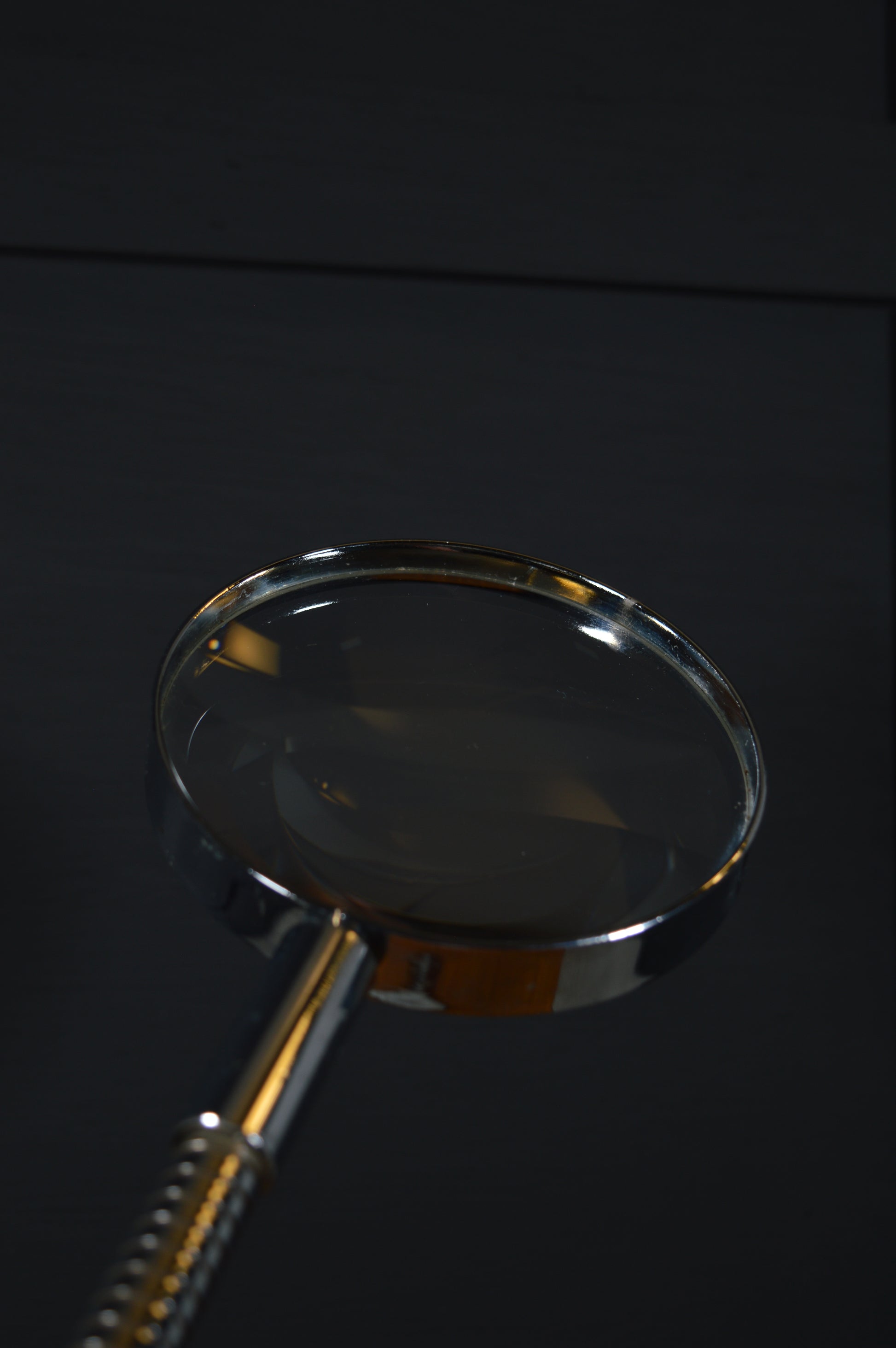 Vintage magnifying glass with metal handle on dark wooden background